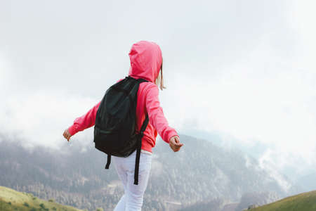 Tween girl with backpack looking on beautiful mountains in the clouds, family travel conceptの写真素材