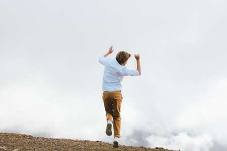 Blonde boy jumping on background of wonderful view of mountain resort, family travel adventure lifestyleの写真素材