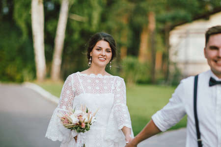 Happy newly married couple, smiling bride brunette young woman with the boho style bouquet with groom, close up portrait outdoorsの写真素材