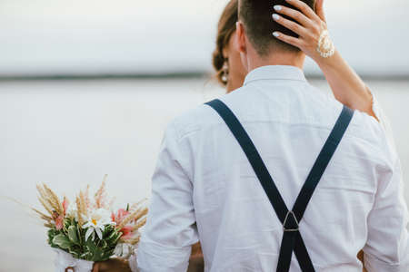Happy newly married couple near lake, bride brunette young woman with boho bouquet, outdoorsの写真素材