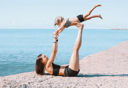 Young fit woman mom with little cute girl exercising on the morning  beach together, healthy lifestyle, sport familyの写真素材