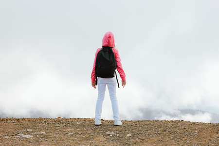 Tween girl with backpack looking on beautiful mountains in the clouds, family travel conceptの写真素材