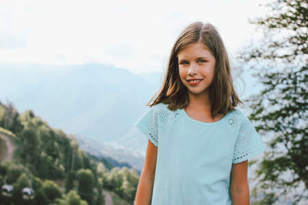 Smiling tween girl looking at camera on background of beautiful mountains, family travel concept adventure lifestyleの写真素材