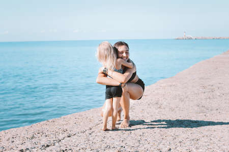 Young fit woman mom with little cute girl exercising on the beach together, healthy lifestyleの写真素材