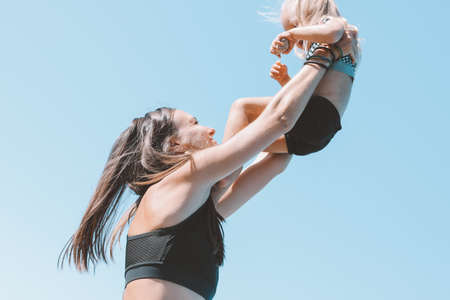 Young fit woman mom with little cute girl exercising on the beach together, healthy lifestyle, dynamic gymnasticの写真素材