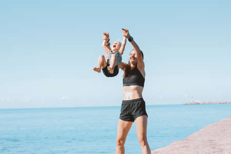 Young fit woman mom with little cute girl exercising on beach together, healthy lifestyle, dynamic gymnasticの写真素材