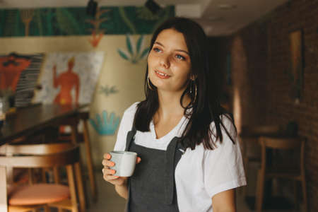 Portrait of smiling charming brunette girl with braces on teeth in casual clothes with cup of coffee  in the cafeの写真素材