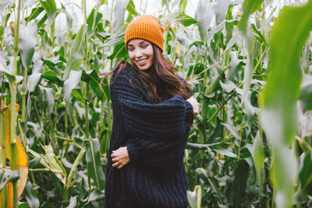 Beautiful carefree long hair asian girl in yellow hat and knitted sweater in autumn corn field. Sensitivity to nature conceptの写真素材