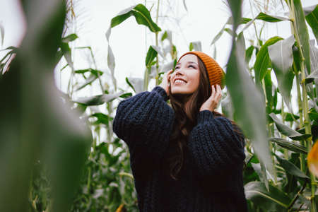 Beautiful carefree long hair asian girl in the yellow hat and knitted sweater in autumn corn field. Sensitivity to nature conceptの写真素材