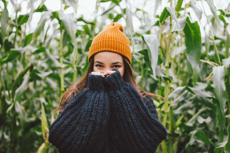 Beautiful carefree long hair asian girl in yellow hat and knitted sweater in autumn corn field. Sensitivity to nature conceptの写真素材