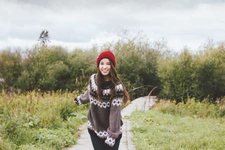 Beautiful carefree long hair asian girl in the red hat and knitted nordic sweater in autumn