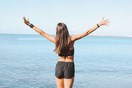 Young slim athletic long hair woman in sportswear doing exercises on the sea beach in the morning,...