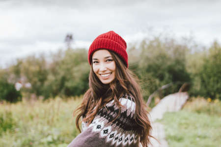 Beautiful carefree long hair asian girl in the red hat and knitted nordic sweater in autumnの写真素材