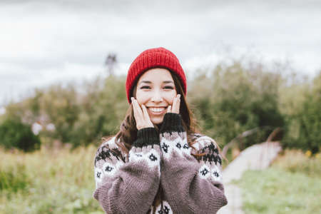 Beautiful carefree long hair asian girl in red hat and knitted nordic sweater in autumn nature parkの写真素材