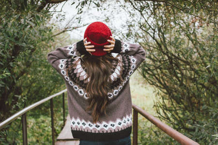 Beautiful carefree long hair asian girl in the red hat and knitted nordic sweater in autumn nature park, travel adventure lifestyleの写真素材