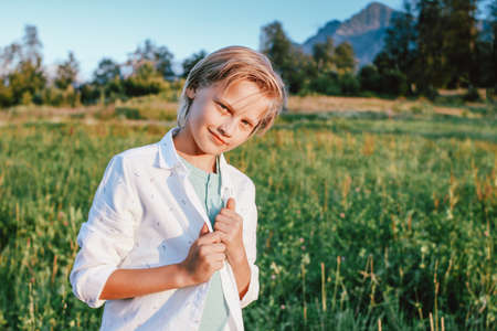 Blonde smiling boy looking at camera on background of wonderful view of green meadow and mountains, family travel adventure lifestyleの写真素材