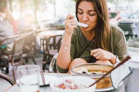 Young smiling brunette girl eating dim sum in a street cafeの写真素材