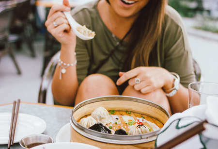 Young smiling brunette girl eating dim sum in a street cafeの写真素材