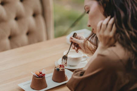 Crop photo of woman eating double tiramisu dessert decorated with fresh berries at the cafeの写真素材