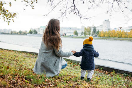 Cute baby boy in fashionable casual clothes explores the world with mother in autumn nature parkの写真素材