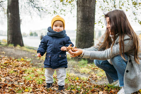 Cute baby boy in fashionable casual clothes explores the world with mother in the autumn nature parkの写真素材