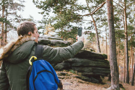 Young male traveler in khaki parka jacket with backpack take photo on his mobile phone, travel adventure の写真素材