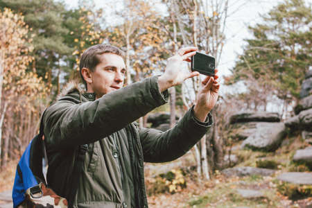 Young male traveler in khaki parka jacket with backpack take photo on his mobile phone, travel...