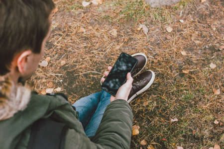 Young male traveler in khaki parka jacket with backpack looks at the route in his mobile phone, travel adventure lifestyleの写真素材