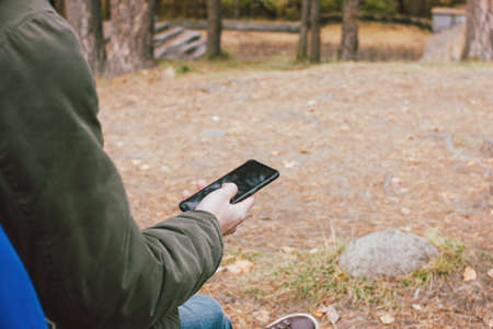 Young male traveler in khaki parka jacket with backpack looks at the route in his mobile phone, travel adventure lifestyleの写真素材
