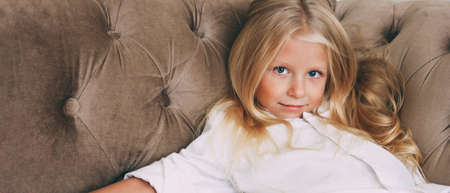 Beauty fashion portrait of smiling little tween girl with fair long hair in white shirt on beige...