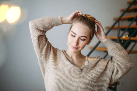 Young beautiful girl with blonde hair in evening beige silk dress and cozy cardigan in front of the...