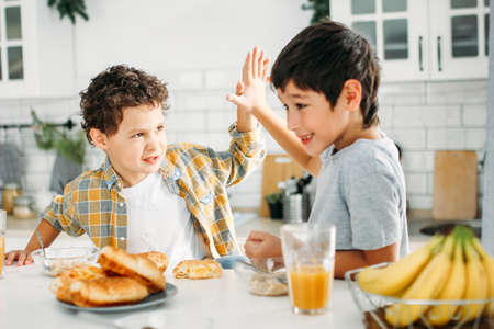 Two siblings tween boys brothers having breakfast on bright kitchen at homeの写真素材