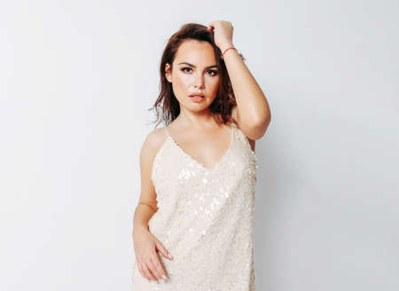 Sensitive beautiful brunette young woman dressed in light evening dress with sequins on white background isolatedの写真素材