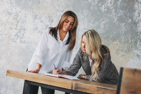 Young successful women colleagues discuss joint project, coaching or mentoring in the modern loft officeの写真素材