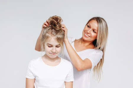 Young beautiful blonde woman make hair style for girl. Joint leisure of mother and daughter....