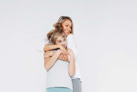 Beautiful blonde mom and daughter preteen in pajamas hugging and having fun isolated on the white backgroundの写真素材