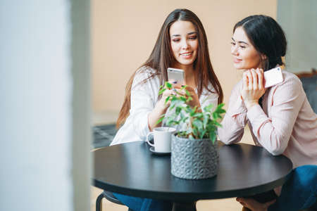 Young carefree brunette girls friends in casual with mobile phones meeting at the bright cafeの写真素材