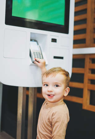 Little cute baby boy child standing next to stand with electronic payment in shopping center or cafeの写真素材