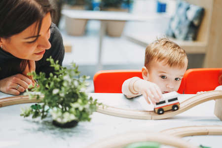 Cute baby boy toddler child with mother play with car toys in game room in shopping mall