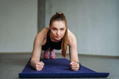 Attractive fit young woman in sport wear girl trains with dumbbells make plank at the loft studio