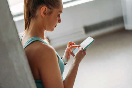 Attractive fit young woman light blue sport wear doing training with mobile at domestic workout class loft studio, fitness healthy lifestyleの写真素材