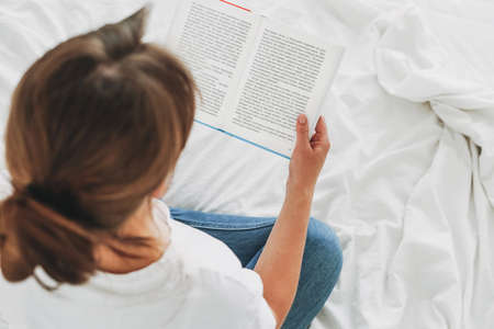 Brunette woman reading book on bed with white linen, view from topの写真素材