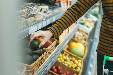 Man takes avocado from shelf in vegetable department at supermarket 