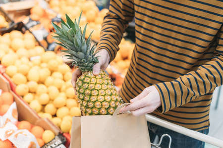 Man in supermarket puts pineapple in paper bagの写真素材