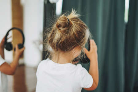 Little toddler girl with fair hair with headphones from behind having fun in studioの写真素材