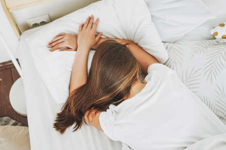 Young woman with long dark hair sleeping in bed with white linen at bright bedroom