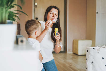 Cute baby boy with mother blowing soap bubbles at home