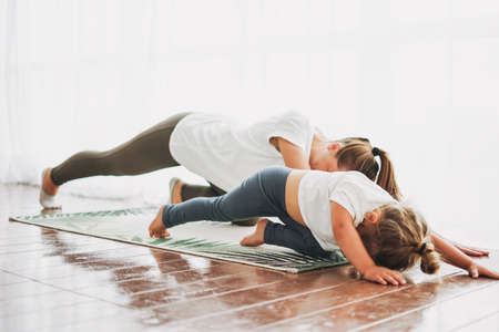 Happy mom and little daughter doing yoga morning exercise together at bright interior homeの写真素材