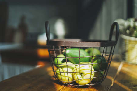 Ripe raw fresh green avocado and apples in metal basket in kitchen, hard sun lightの写真素材