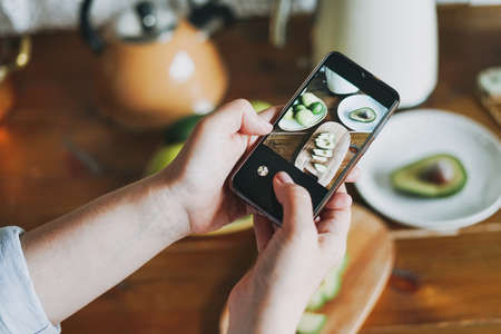 Woman take smartphone photo of still life of fresh avocado on wooden tableの写真素材